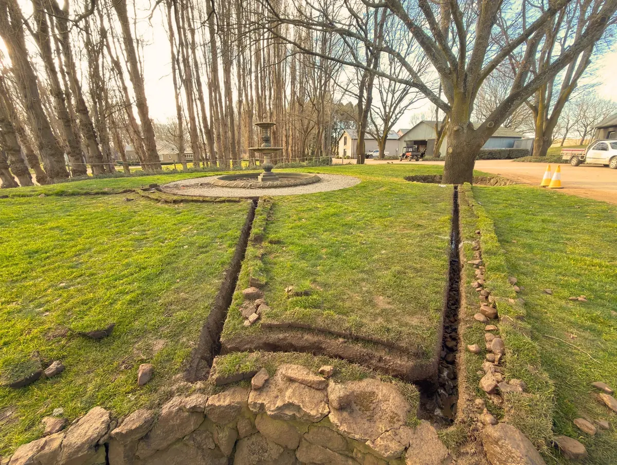 A narrow trench across established lawn beneath mature trees
