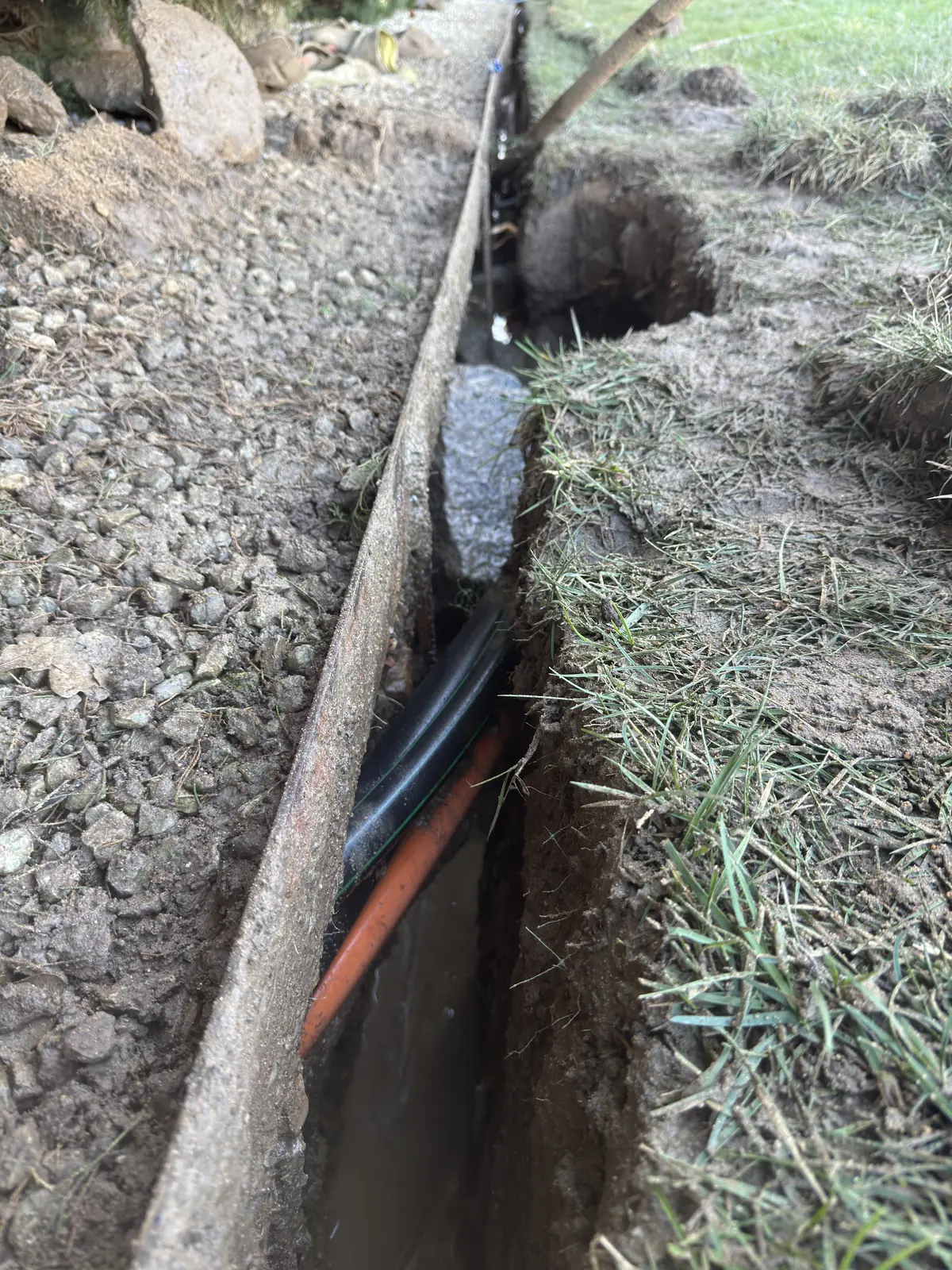 A vacuum hose beside exposed utility services in a trench