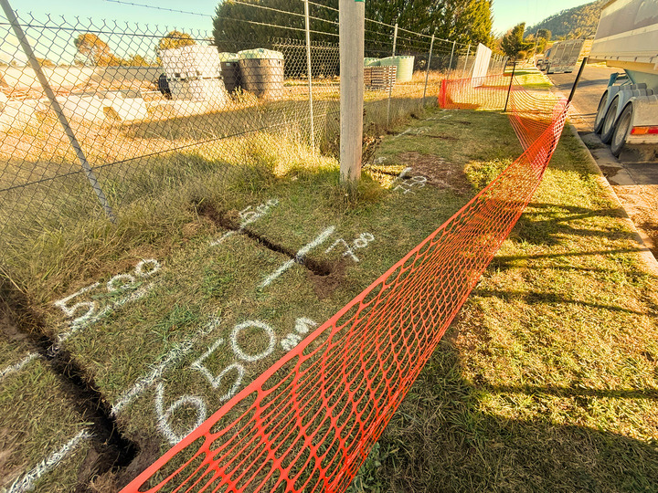 Marked underground service route beside a secured excavation area